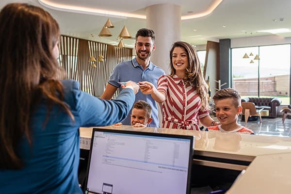Familie mit zwei Kindern am Empfang eines Hotels, während sie eine Schlüsselkarte erhalten.