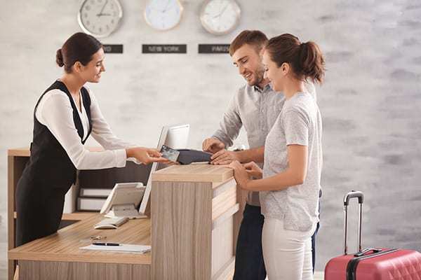Hotelmitarbeiterin an der Rezeption übergibt den Gästen ihre Schlüsselkarte mit Gepäck im Hintergrund.